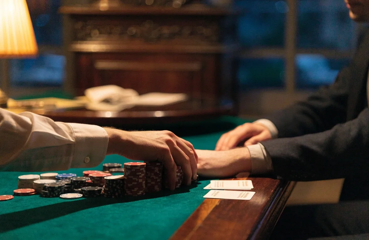 Dłoń na filcu stołu pokerowego pod lampą, karty odwrócone